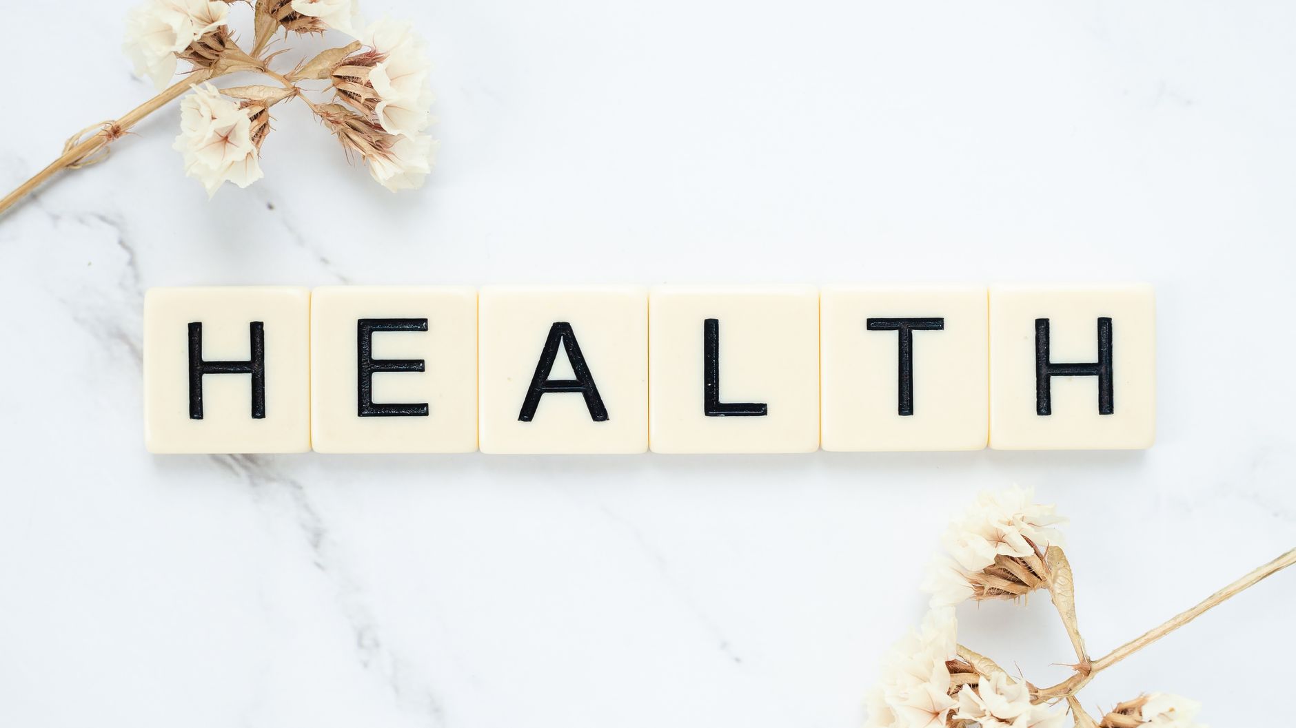 Creative arrangement of scrabble tiles spelling 'Health' with white flowers on a marble surface. — 8 Methods to Debunk Wellne