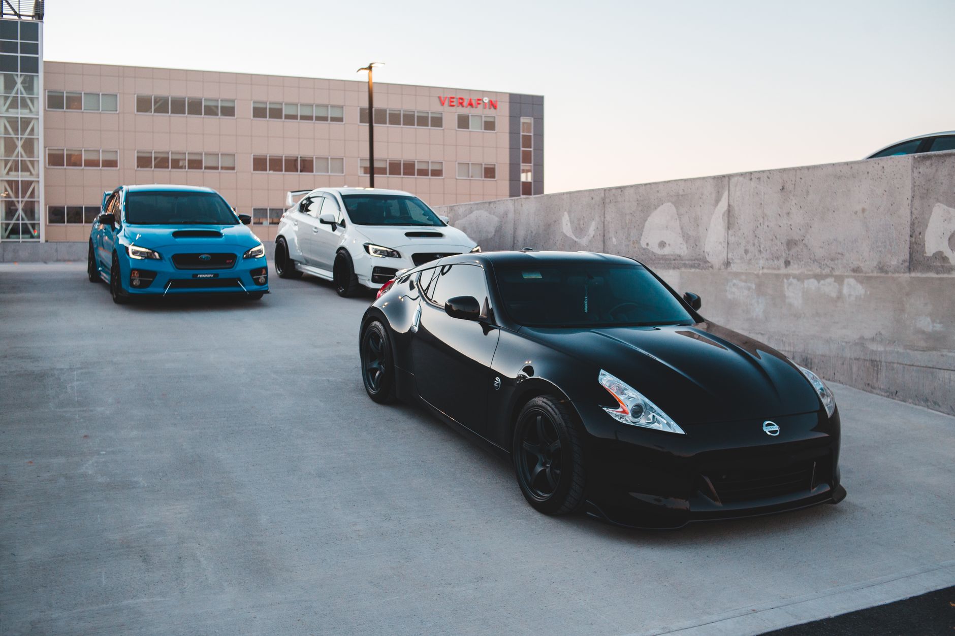 Sports cars parked on concrete road near wall against non residential building and clear sky at sunset — Automotive Advertisi