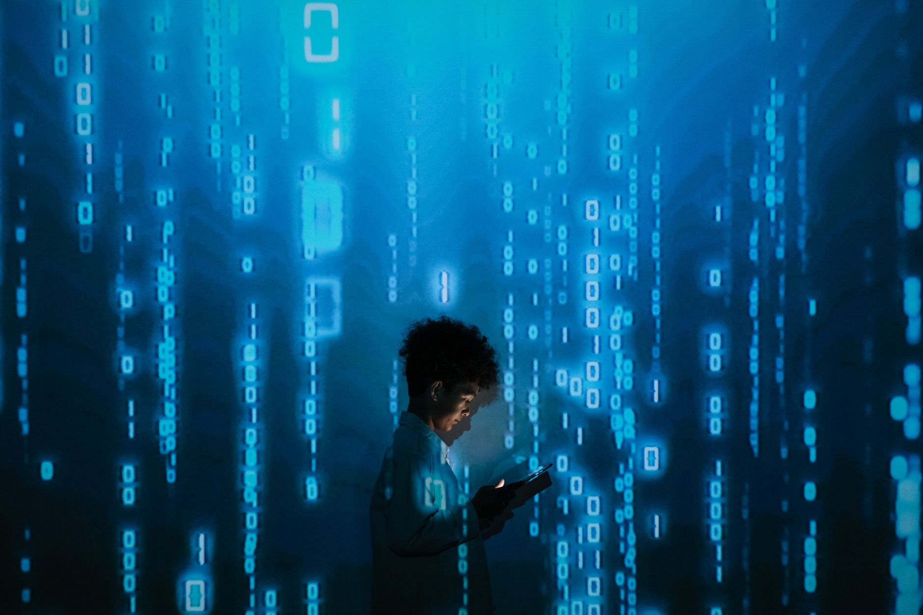 Silhouette of a person using a smartphone surrounded by digital binary code projections. — Ban Technology In the Classroom -