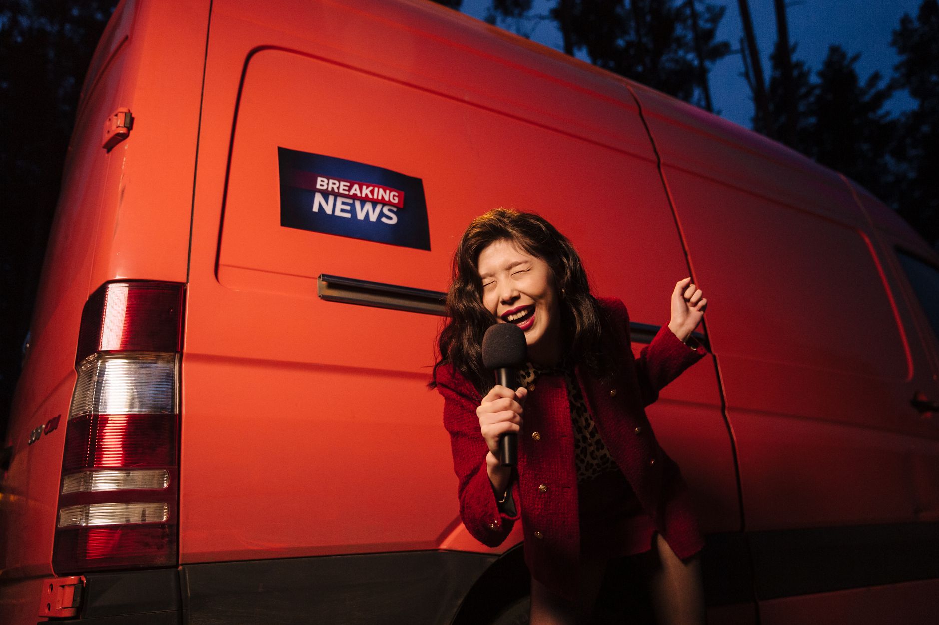 Asian woman reporter energetically broadcasting with a microphone in front of a news van at night. — Dream Vegas Casino Onlin