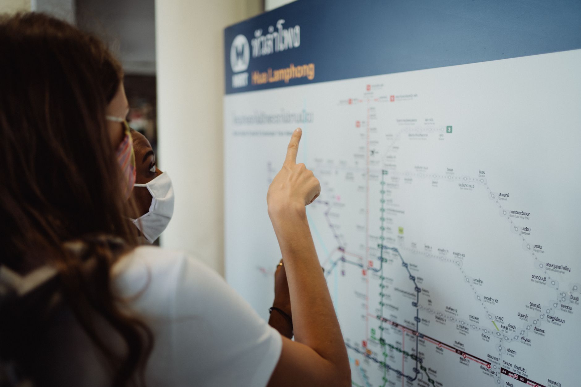 Two women in face masks pointing at a transport map, exploring new directions. — How to reserve your Travel Online