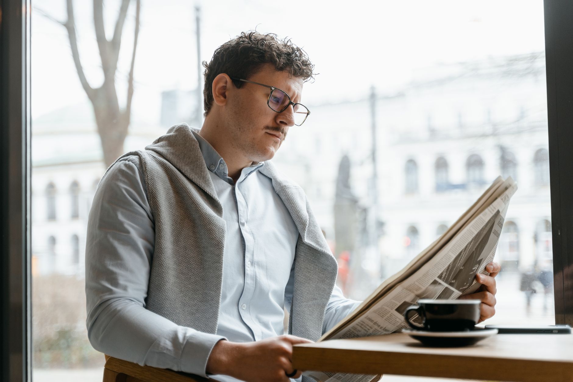Adult man reads a newspaper by a café window, enjoying a coffee break indoors. — Need To Get Enrolled In An Online Football P