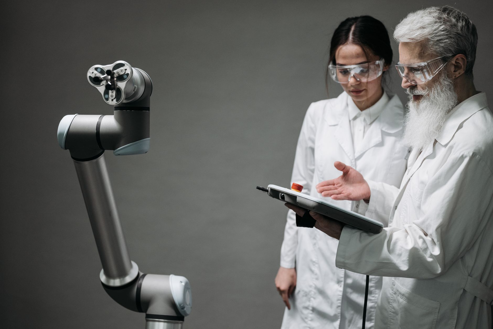 Researchers in lab coats and safety glasses engaging with a robotic arm in a lab setting. — Results of 3G Technology