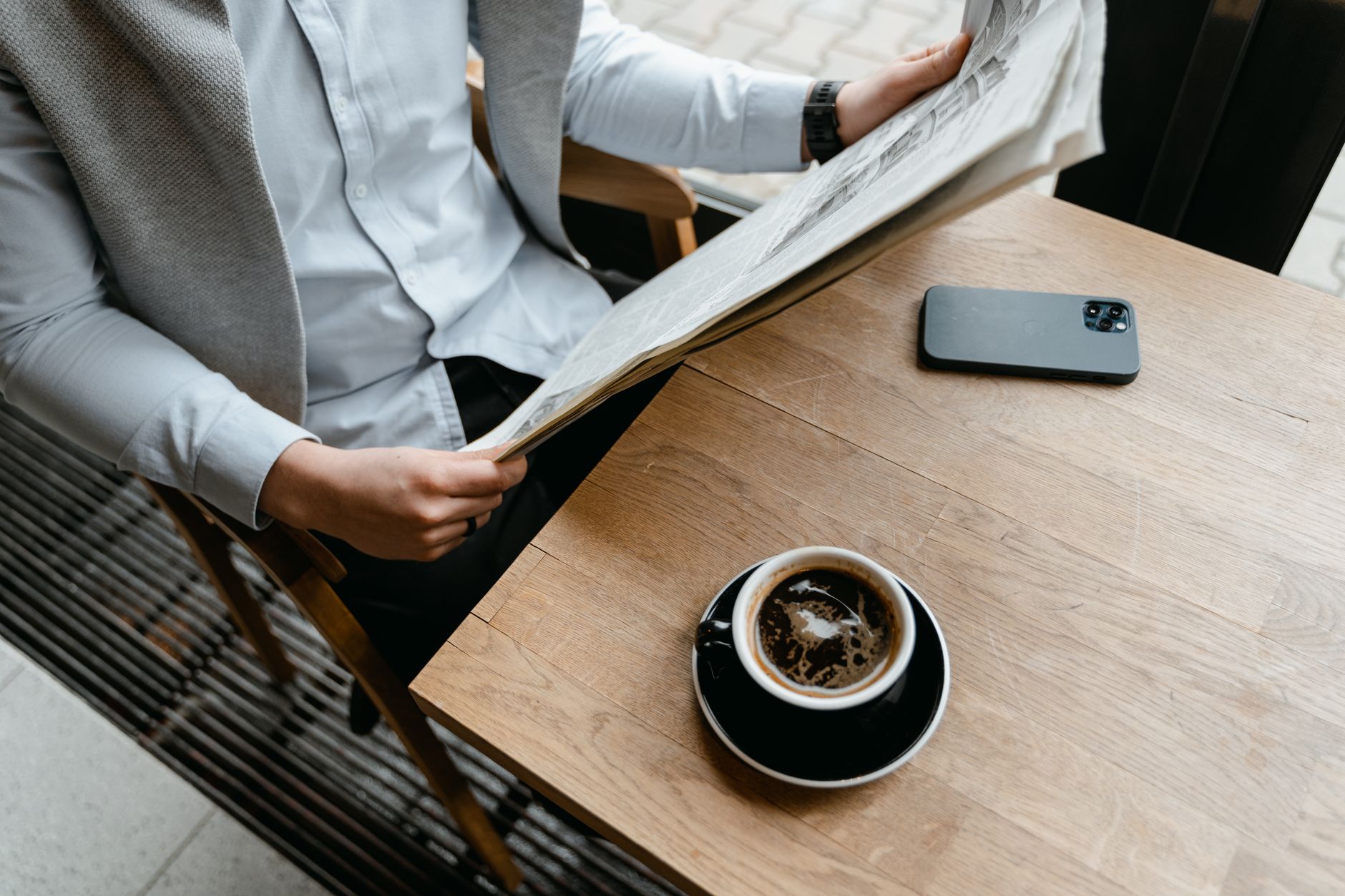 An adult male enjoying his coffee while reading a newspaper at a cafe with his smartphone nearby. — How to get every