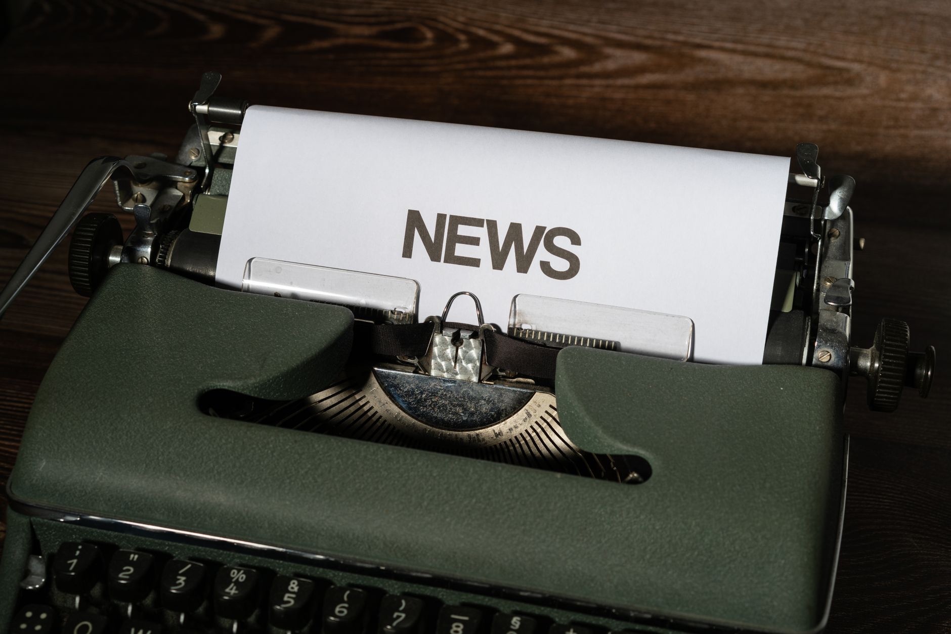 A retro typewriter featuring a 'NEWS' headline typed on white paper against a wooden surface. — Strategies for Winnin