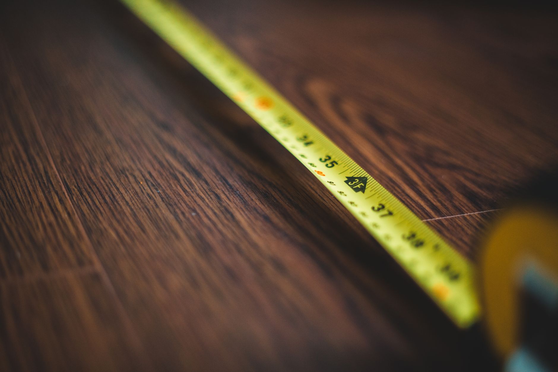 Yellow tape measure extended across a dark wooden floor, highlighting measurement details. — Vinyl Substitute Window - Afford