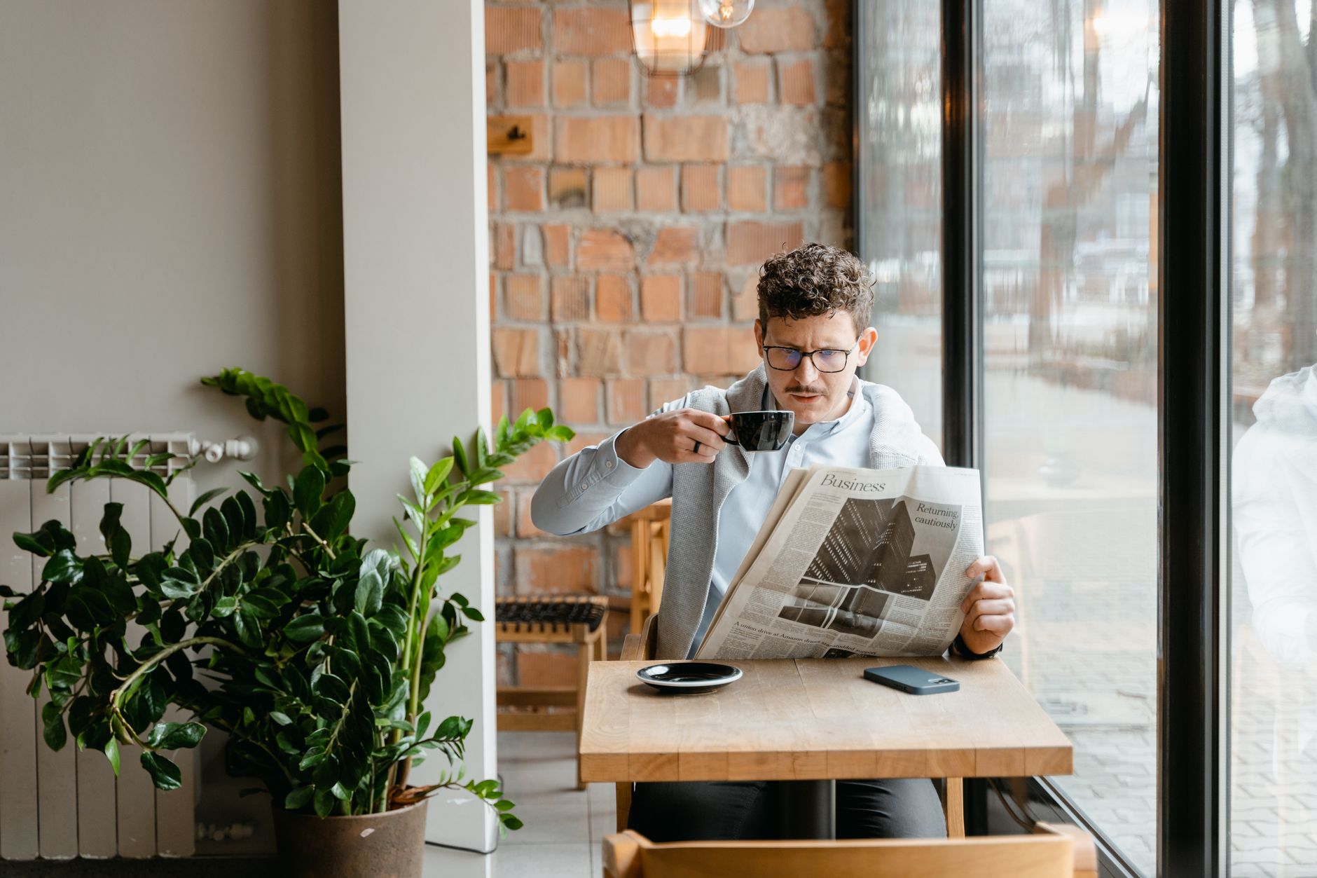 Man sitting indoors with coffee and newspaper, surrounded by plants by the window. — Weed filters: Enhancing Your Smoking Exp